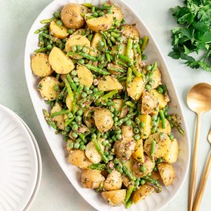A platter of vegan Asparagus Potato Salad, with serving utensils, ready to serve.