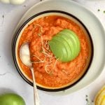 A bowl of vegan pumpkin soup, garnished with a sliced apple.