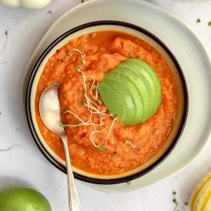 A bowl of vegan pumpkin soup, garnished with a sliced apple.
