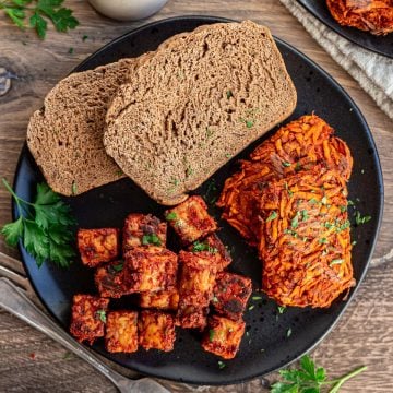 A plate of sweet potato hash browns, tempeh sausage, and toast.