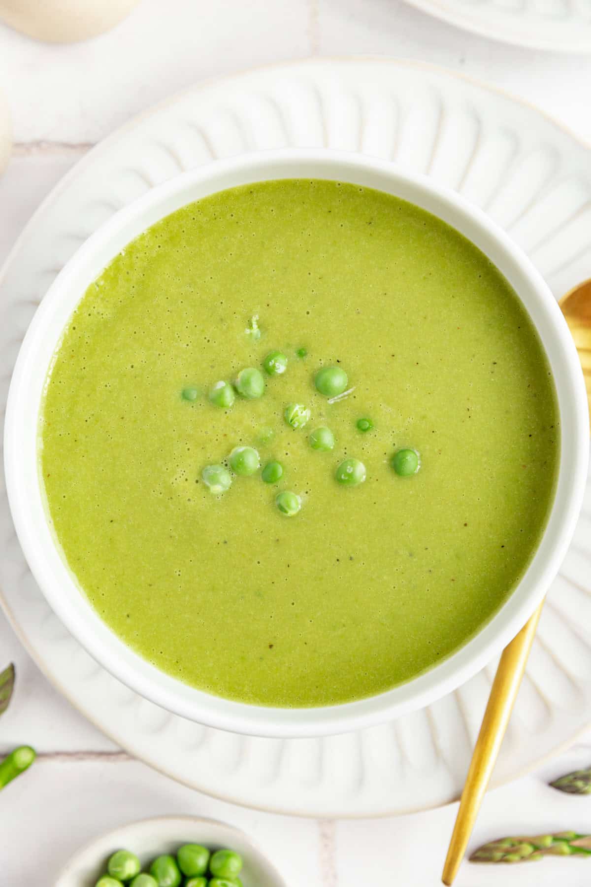 A bowl of Vegan Asparagus Soup garnished with fresh peas.