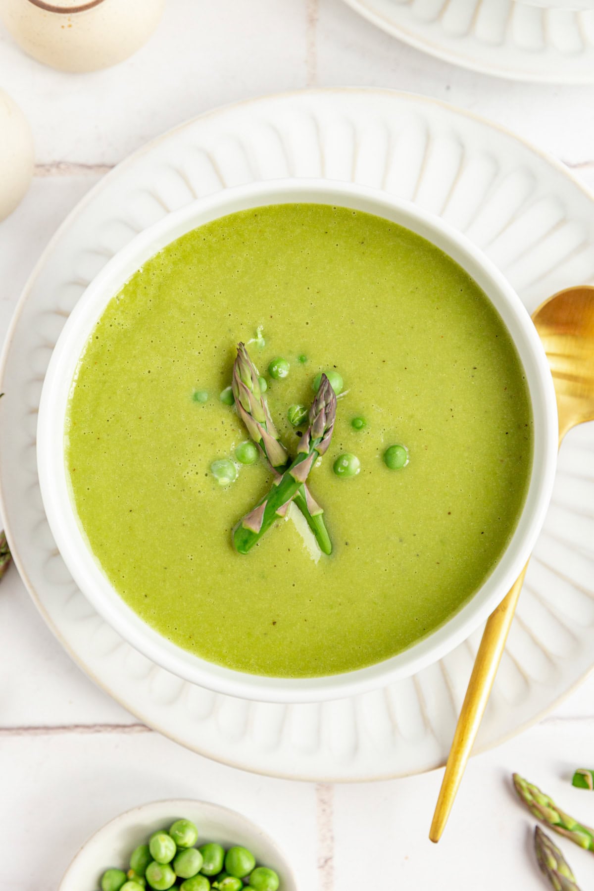 A bowl of Vegan Asparagus Soup, garnished with fresh peas and two raw asparagus spears.