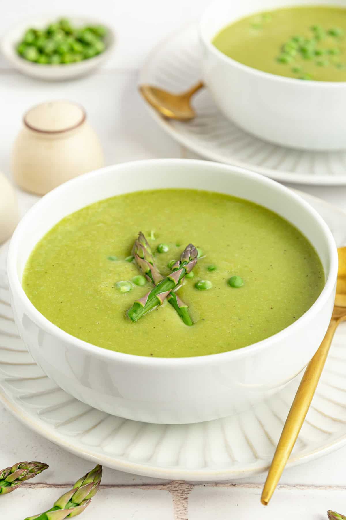 Two bowls of Vegan Asparagus Soup, with spoons resting on plates, ready to serve.