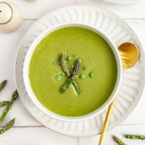 A bowl of Vegan Asparagus Soup on a plate, with a spoon, ready to serve.