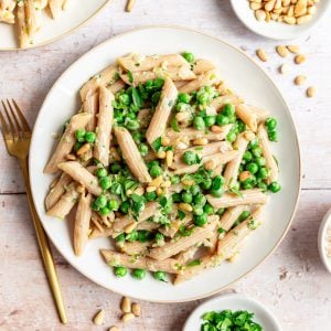 A plate of Vegan Pea and Spring Onion Pasta with bowls of garnishes surrounding it.
