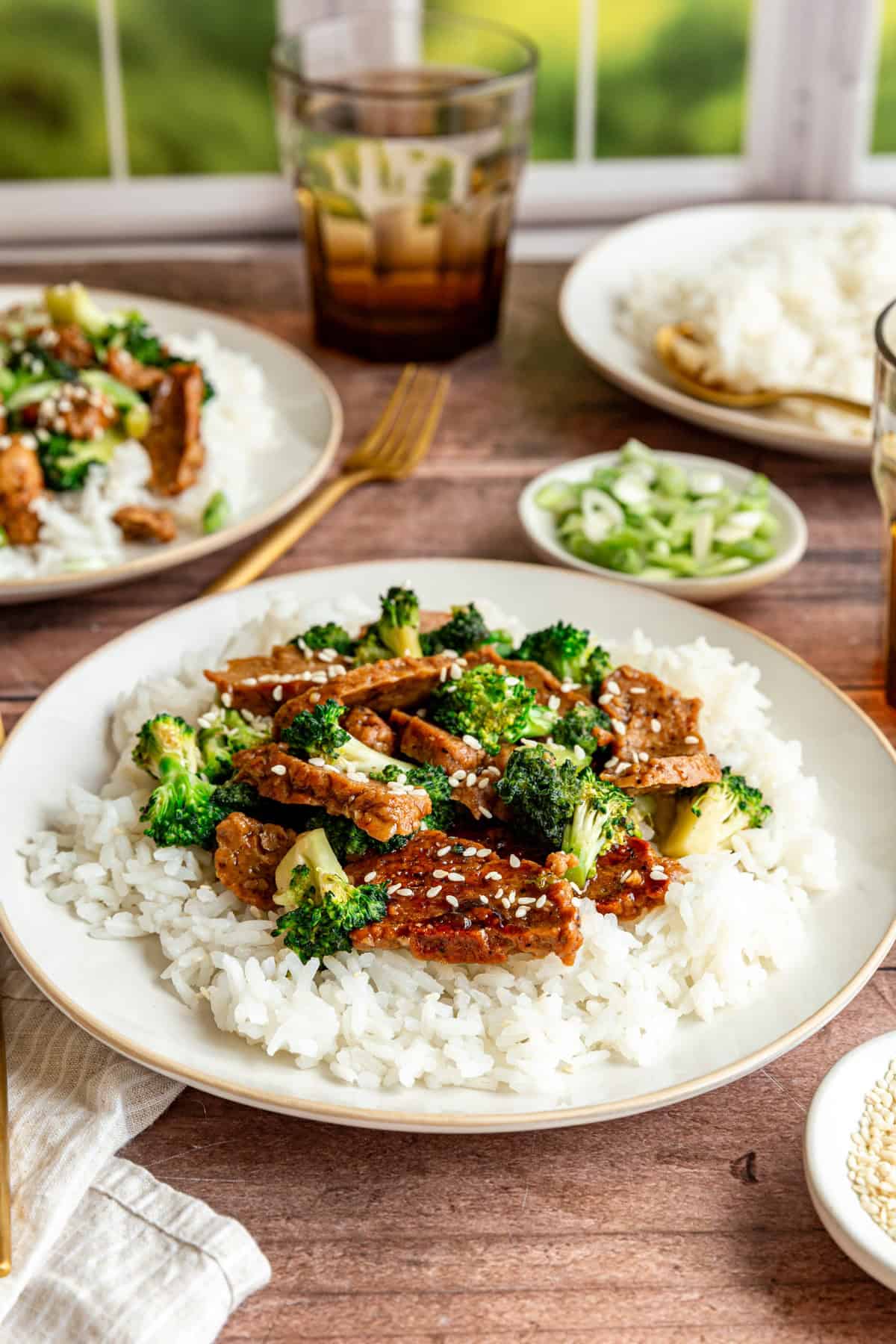 A table with several plates of teriyaki and cups of water.