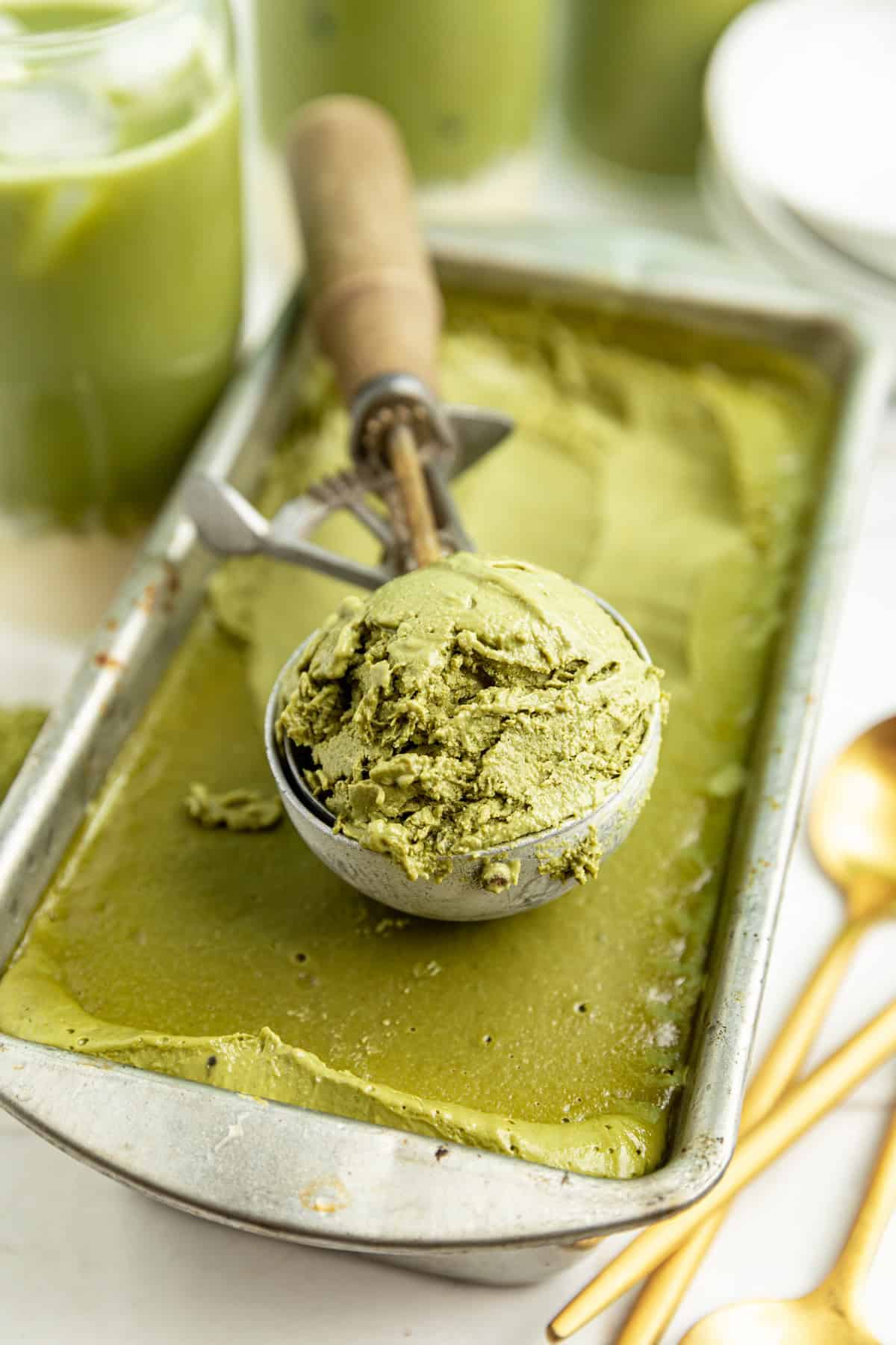 A container of vegan matcha ice cream with an ice cream scoop.