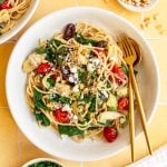 A bowl of vegan mediterranean pasta, with a fork and spoon, ready to serve.