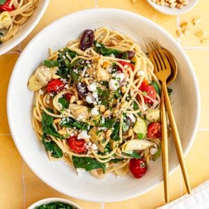 A bowl of vegan mediterranean pasta, with a fork and spoon, ready to serve.