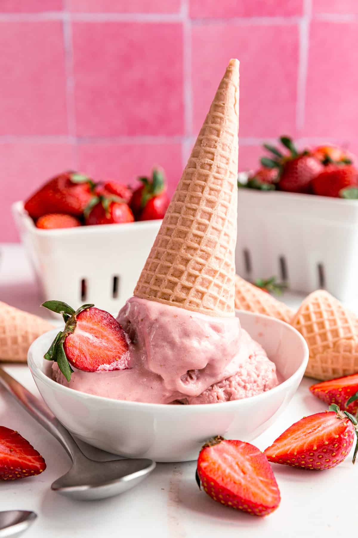A bowl with several scoops of Vegan Strawberry Ice Cream, and an upside down ice cream cone sticking into the bowl.