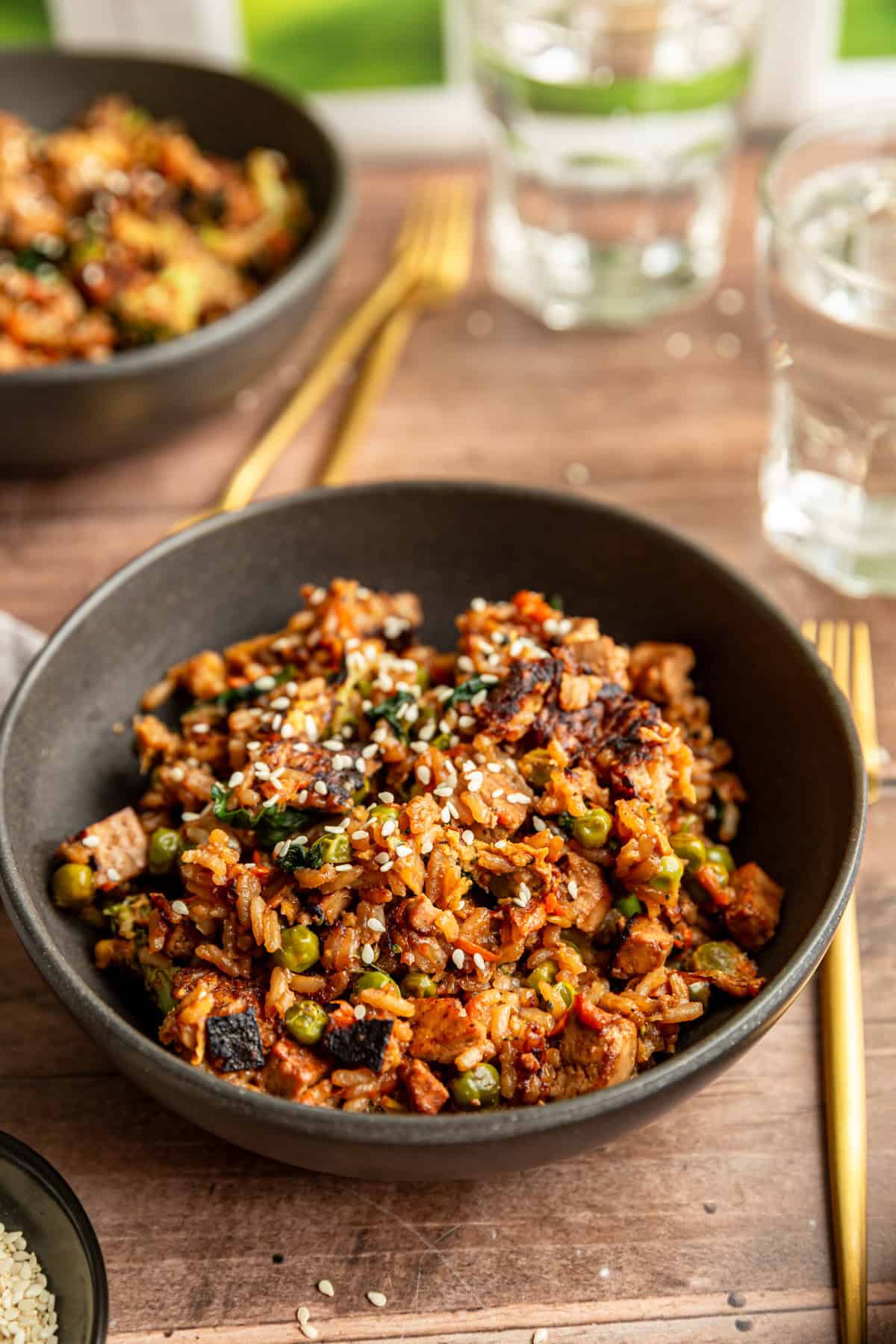 Two bowls of vegan fried rice, with glasses of water, ready to eat.