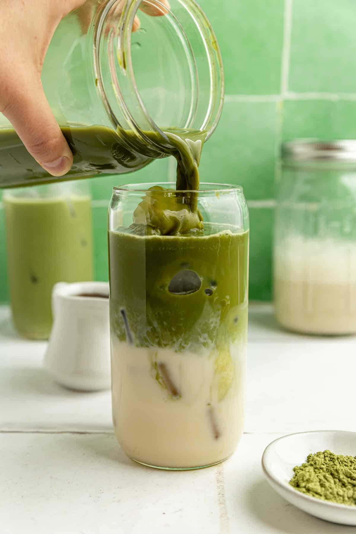 Matcha being poured into a class with ice and milk.
