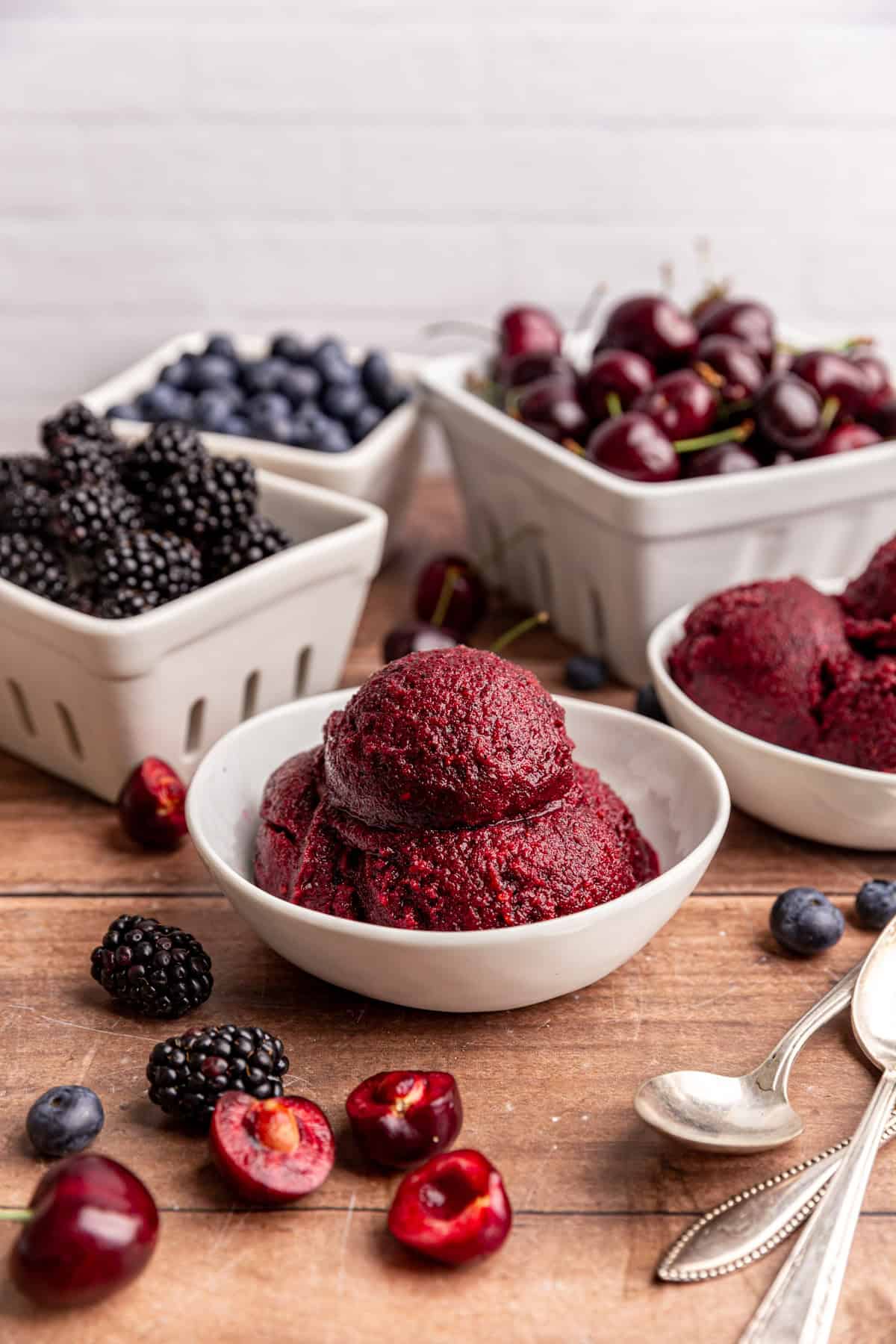 A bowl of creamy berry sorbet, with berry baskets of blueberries, blackberries, and cherries.