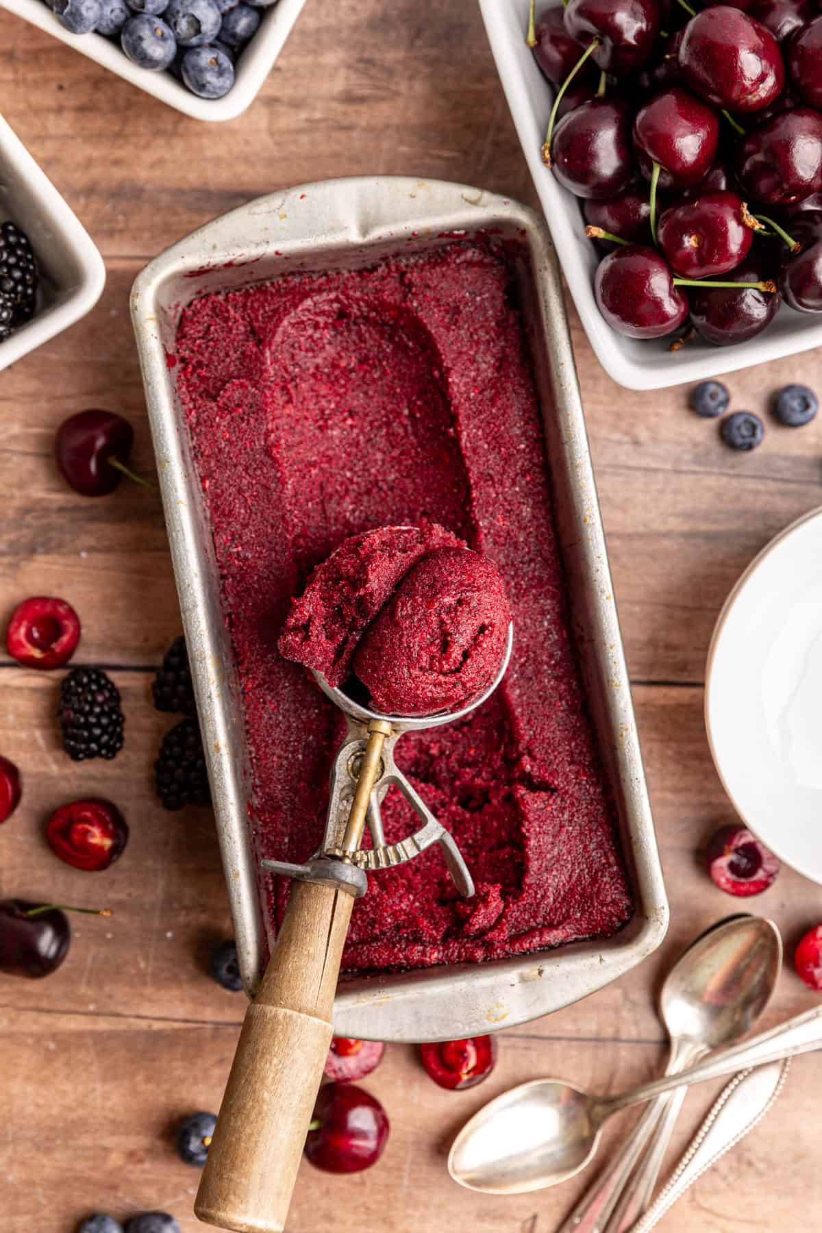 A loaf pan of creamy berry sorbet, with a scoop of sorbet freshly scooped.