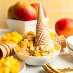 A bowl of no-churn vegan mango ice cream with an upside-down ice cream cone in the bowl.
