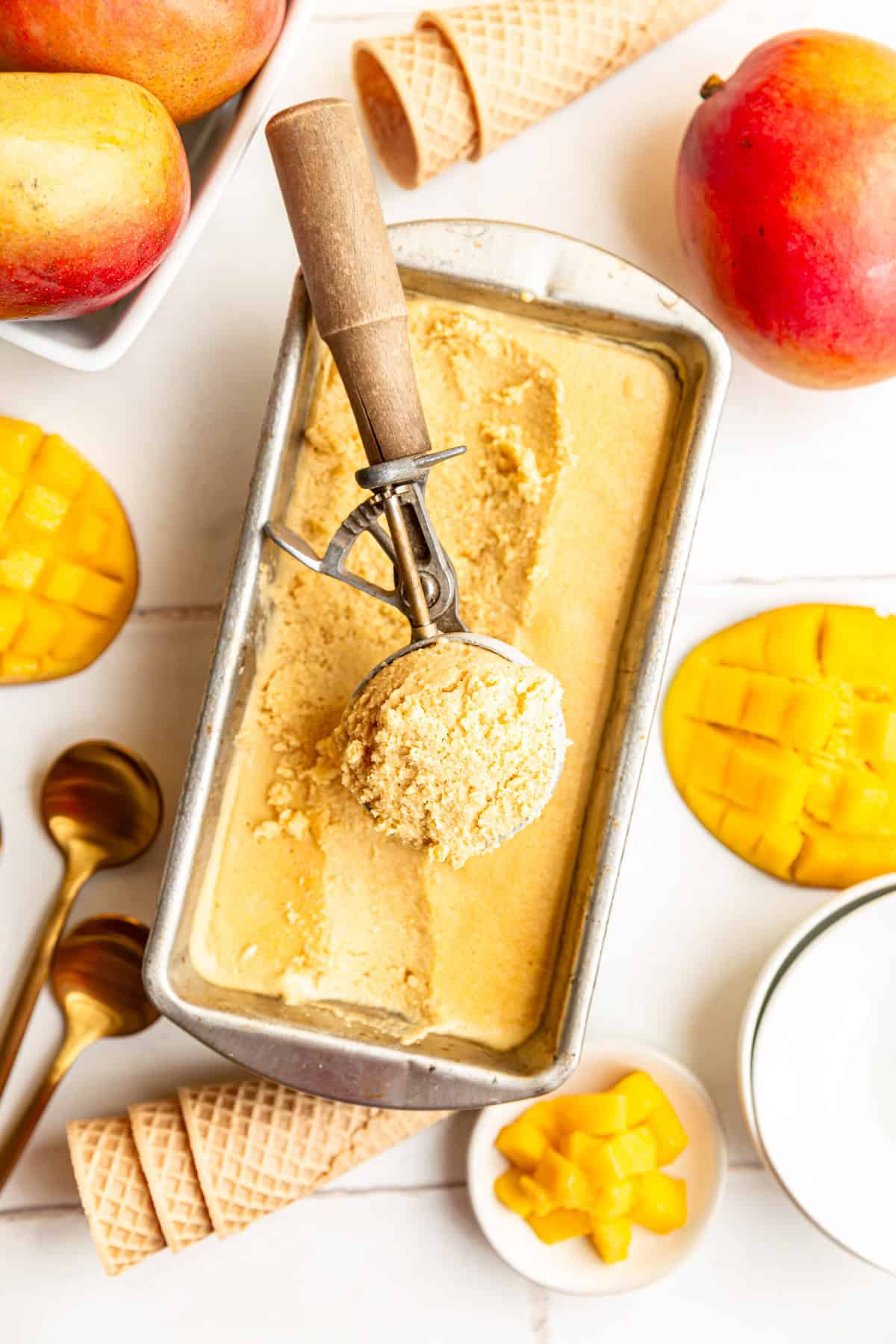 A container of mango ice cream with an ice cream scoop scooping out some ice cream.