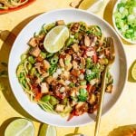 A bowl of zoodle pad thai, garnished with a lime wedge, with a fork, ready to eat.
