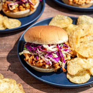 A bbq tempeh sandwich on a plate with chips.