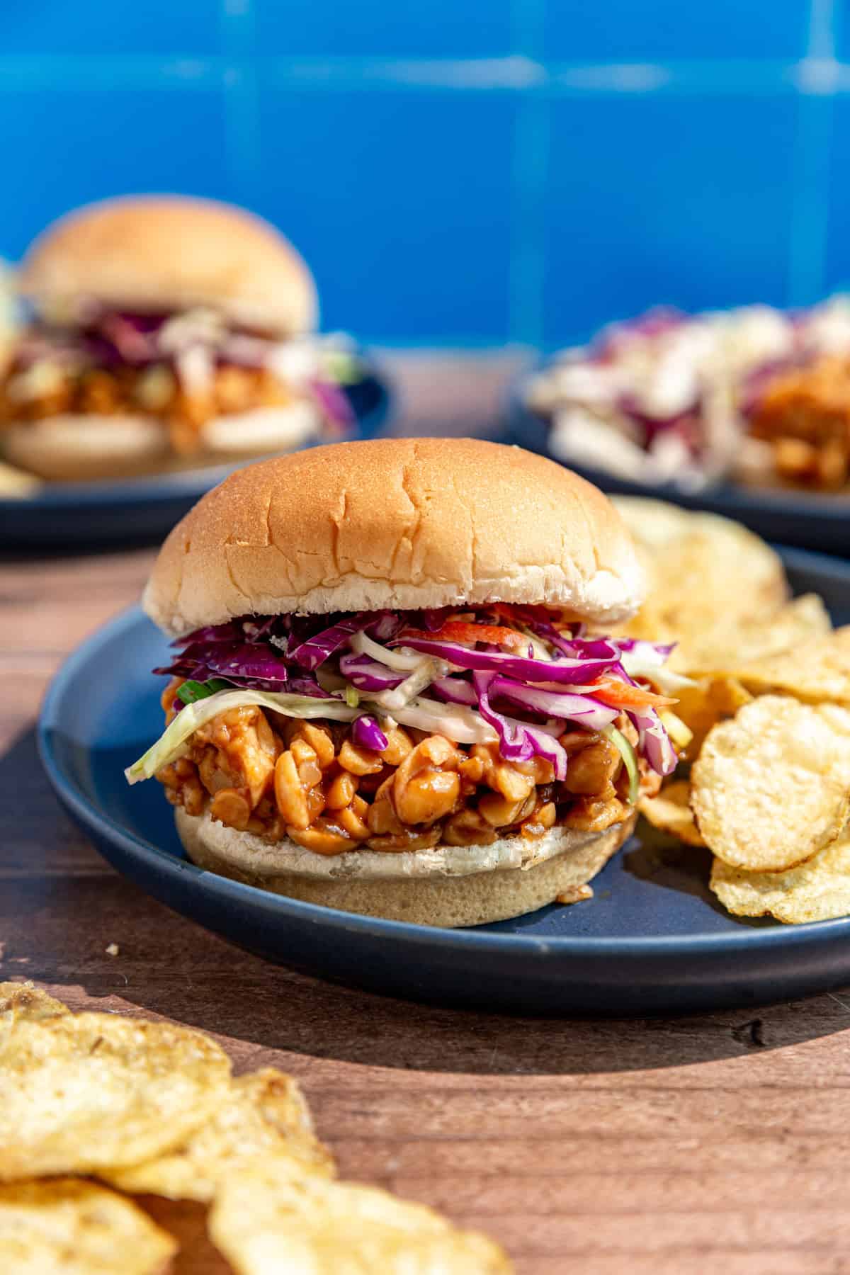 A bbq tempeh sandwich, with coleslaw on the sandwich, and chips on the side.