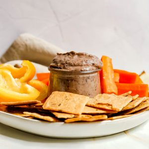 A jar of black bean dip on a plate of veggies and crackers.