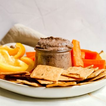 A jar of black bean dip on a plate of veggies and crackers.
