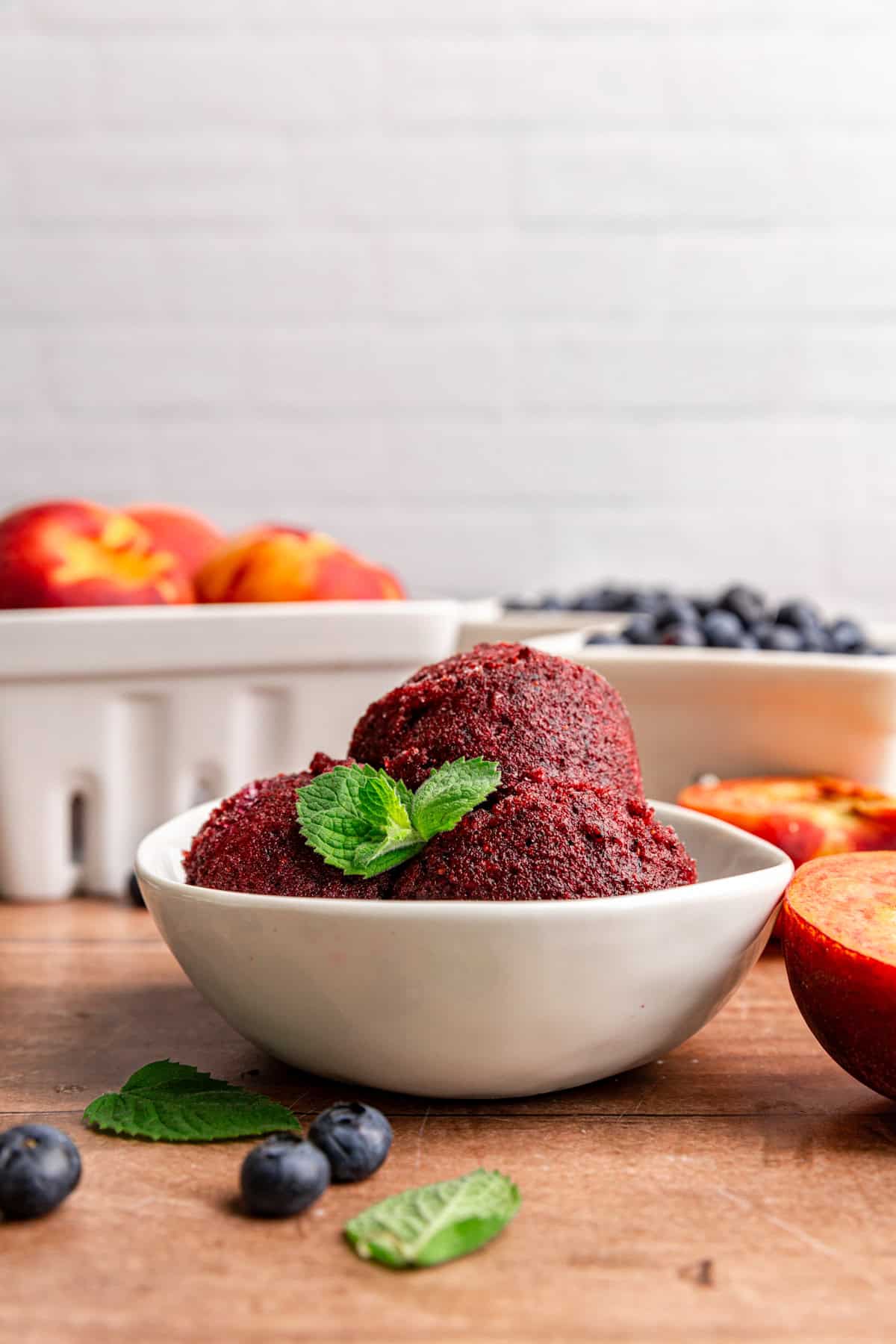 A bowl of Blueberry Peach Sorbet, on a table with containers of blueberries and peaches.