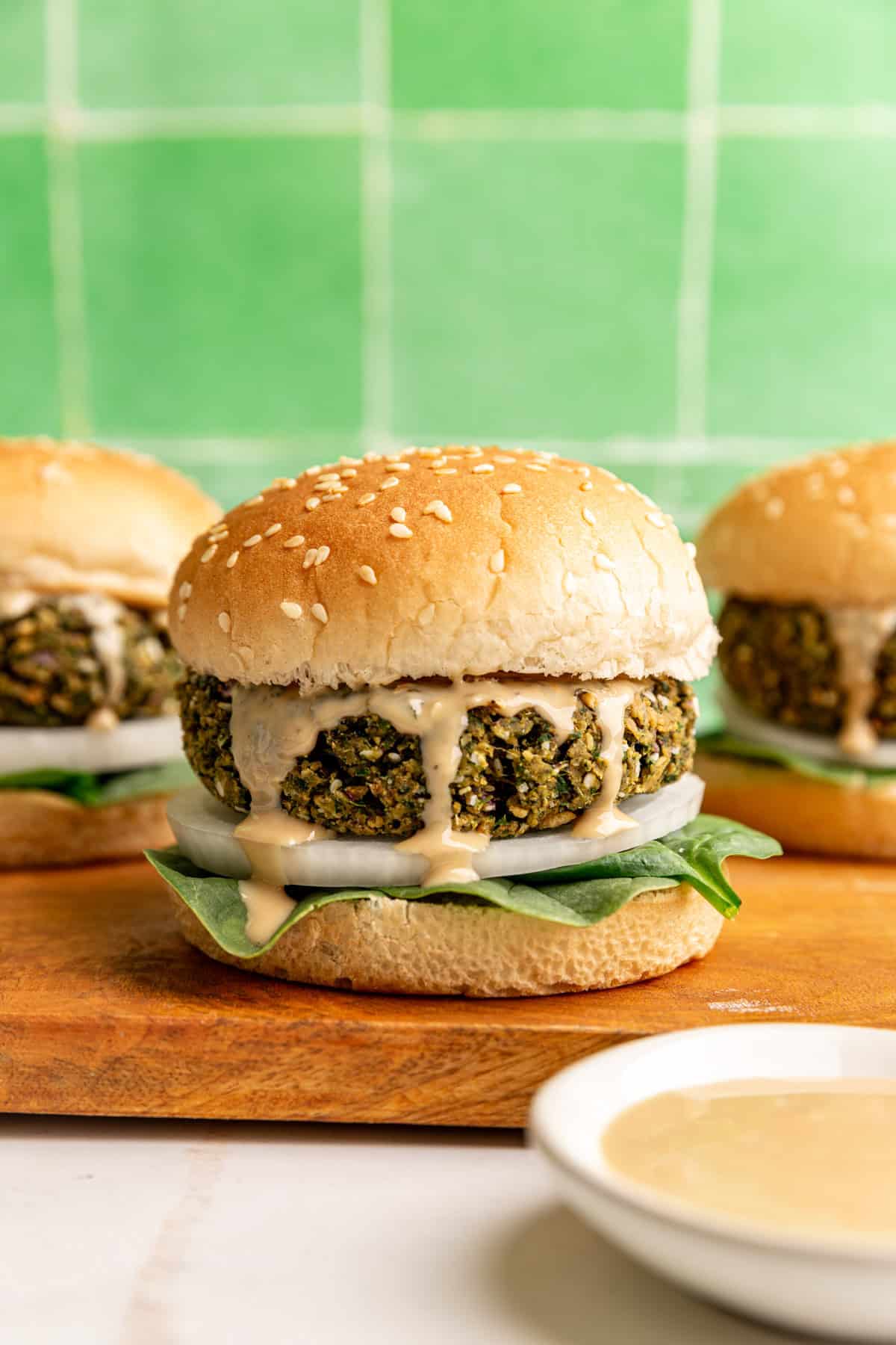A falafel burger served on a bun, with spinach, onion, and tahini.