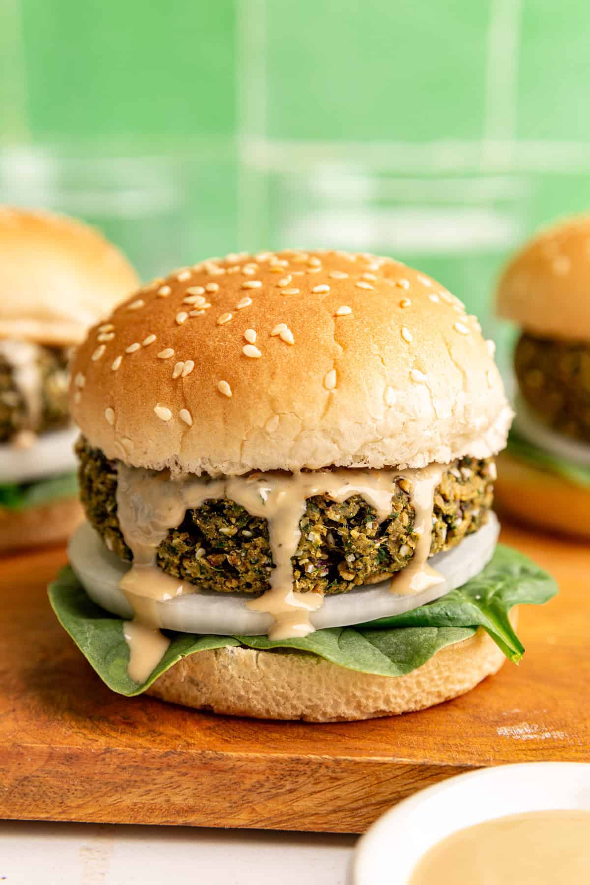 A falafel burger served on a bun, with spinach, onion, and tahini.