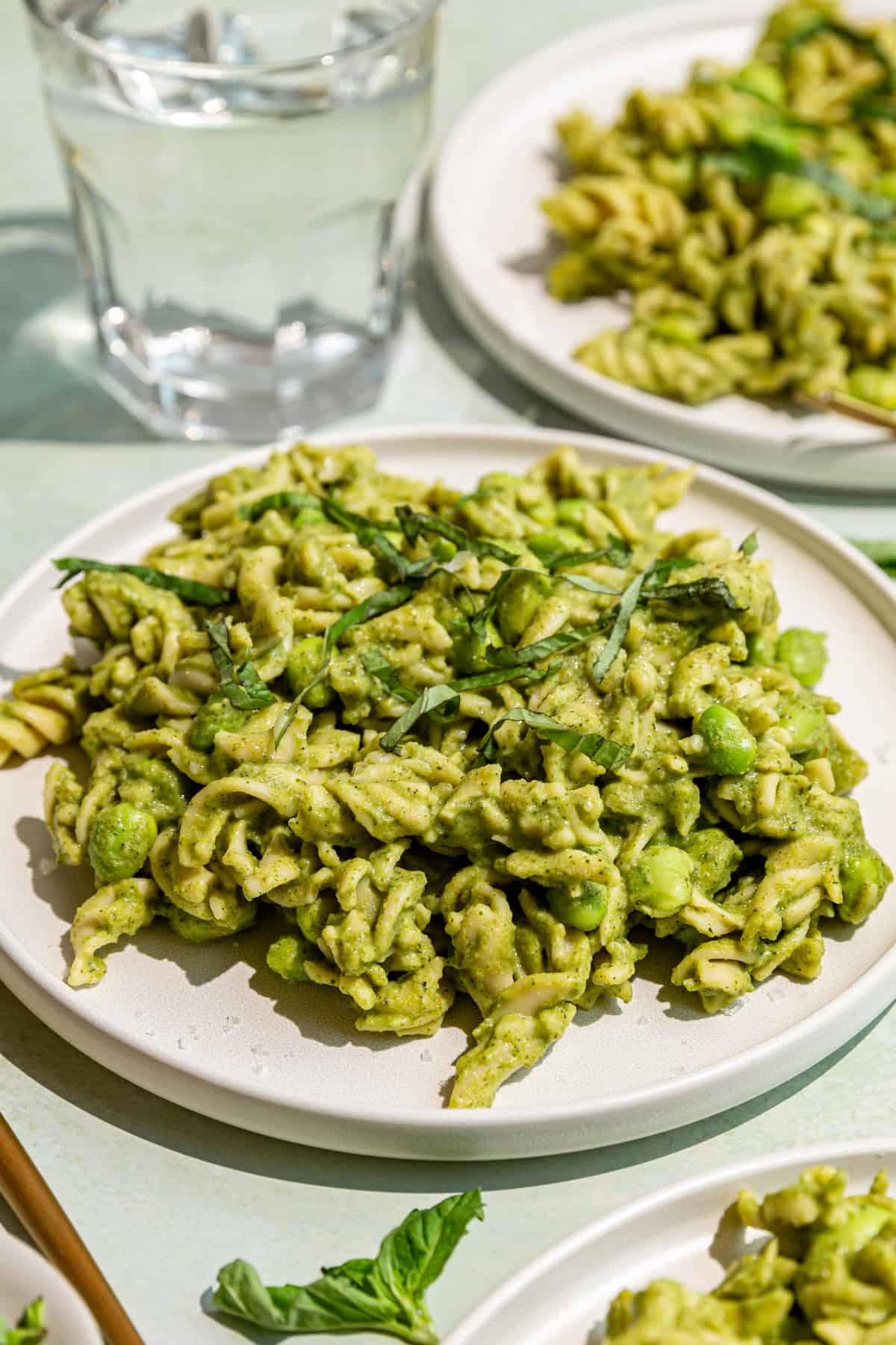 Two plates of broccoli pasta sauce and pasta, with a glass of water, ready to eat.