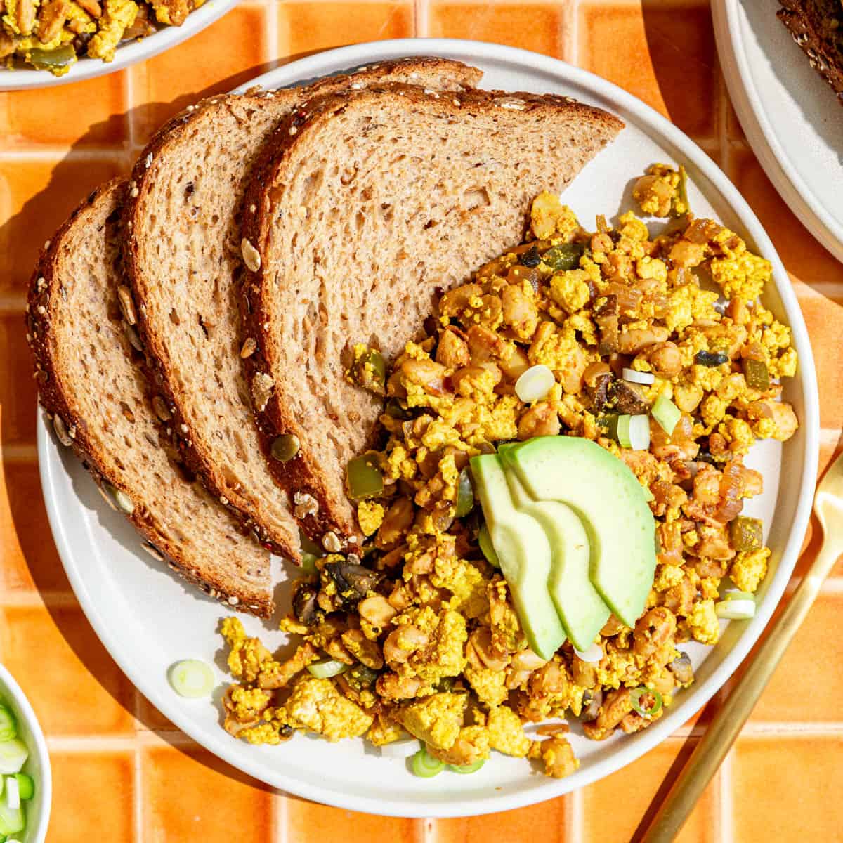 A plate of Scrambled Tempeh, topped with avocado, and served with toast.