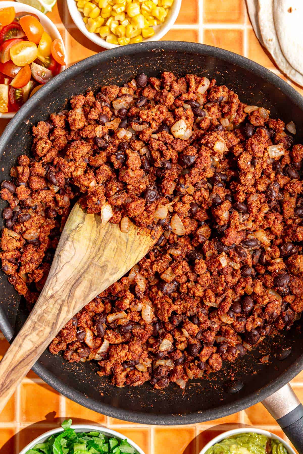 A pan of seitan taco meat, with toppings surrounding it, ready to make tacos.