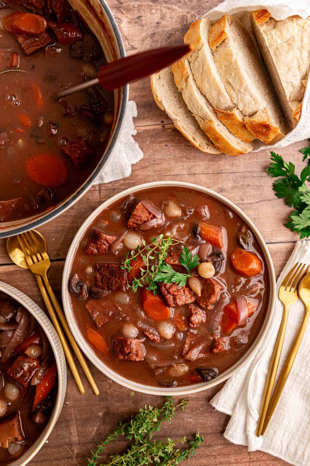 A pot of vegan beef Bourguignon with two bowls full of stew, ready to serve.