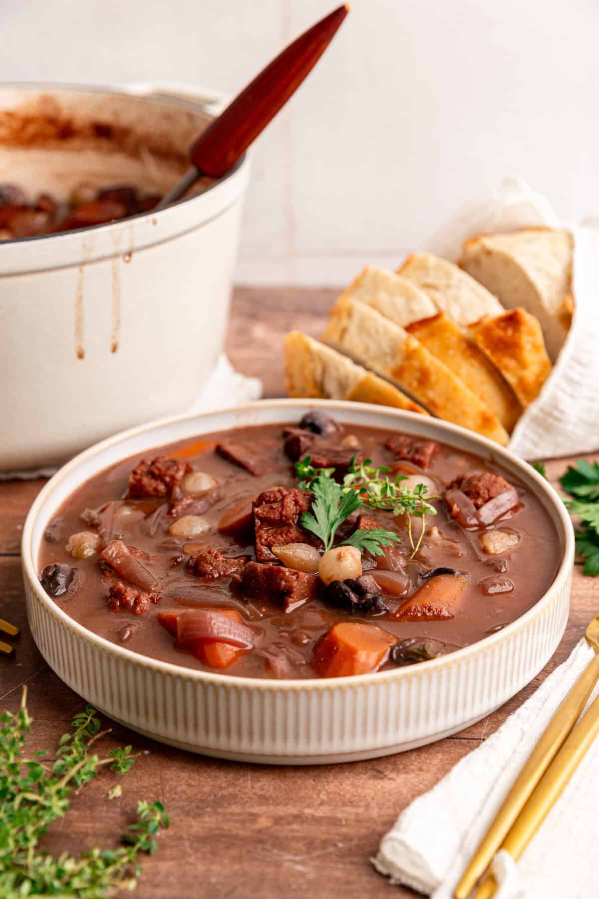 A bowl of beef bourguignon with the pot of stew behind it.