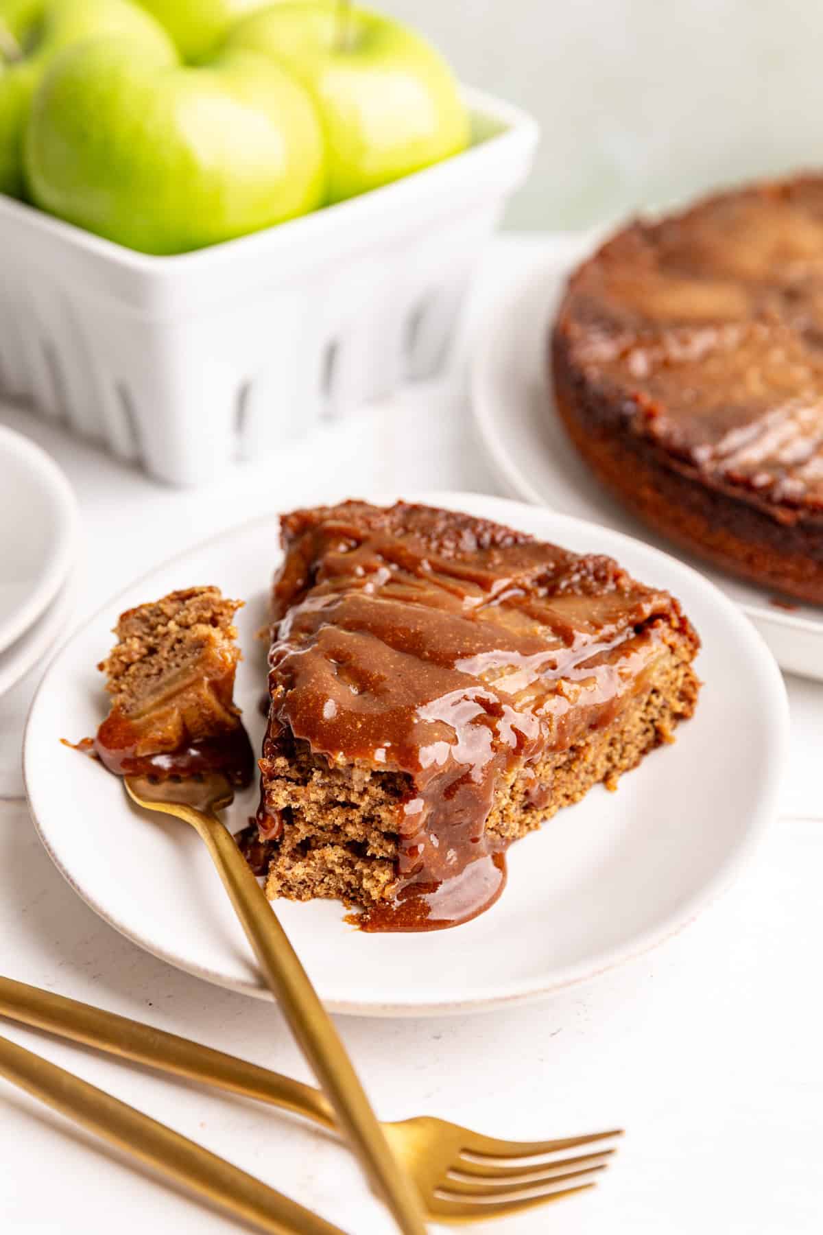 A slice of Vegan Apple Upside Down Cake, with a drizzle of caramel on top, and a bite taken out.