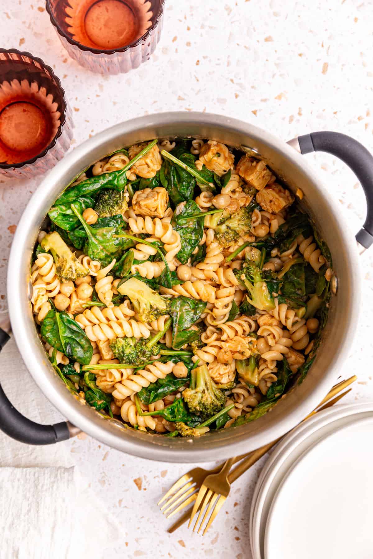 A pot of vegan creamy spinach pasta with several plates, forks, and glasses surrounding it. Ready to serve.