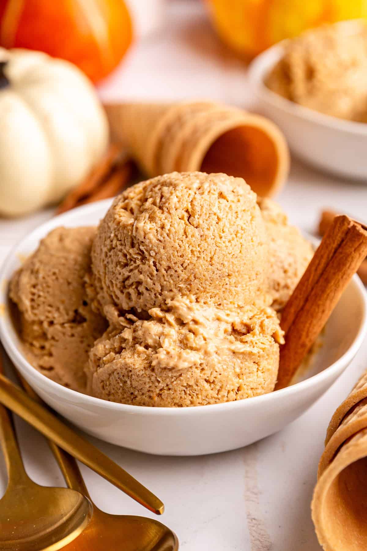 A bowl of several scoops of vegan pumpkin pie ice cream and a cinnamon stick.