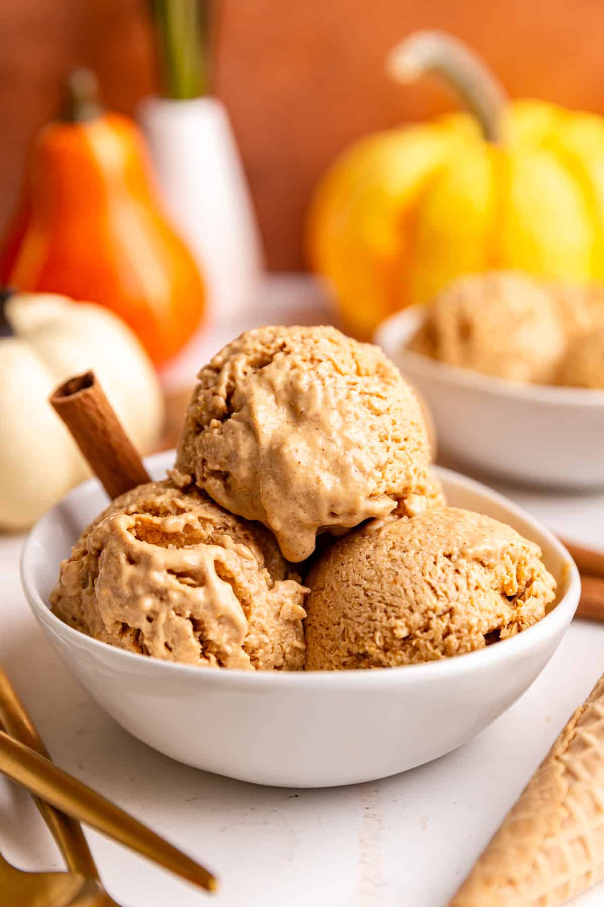 A bowl of several scoops of vegan pumpkin pie ice cream and a cinnamon stick.