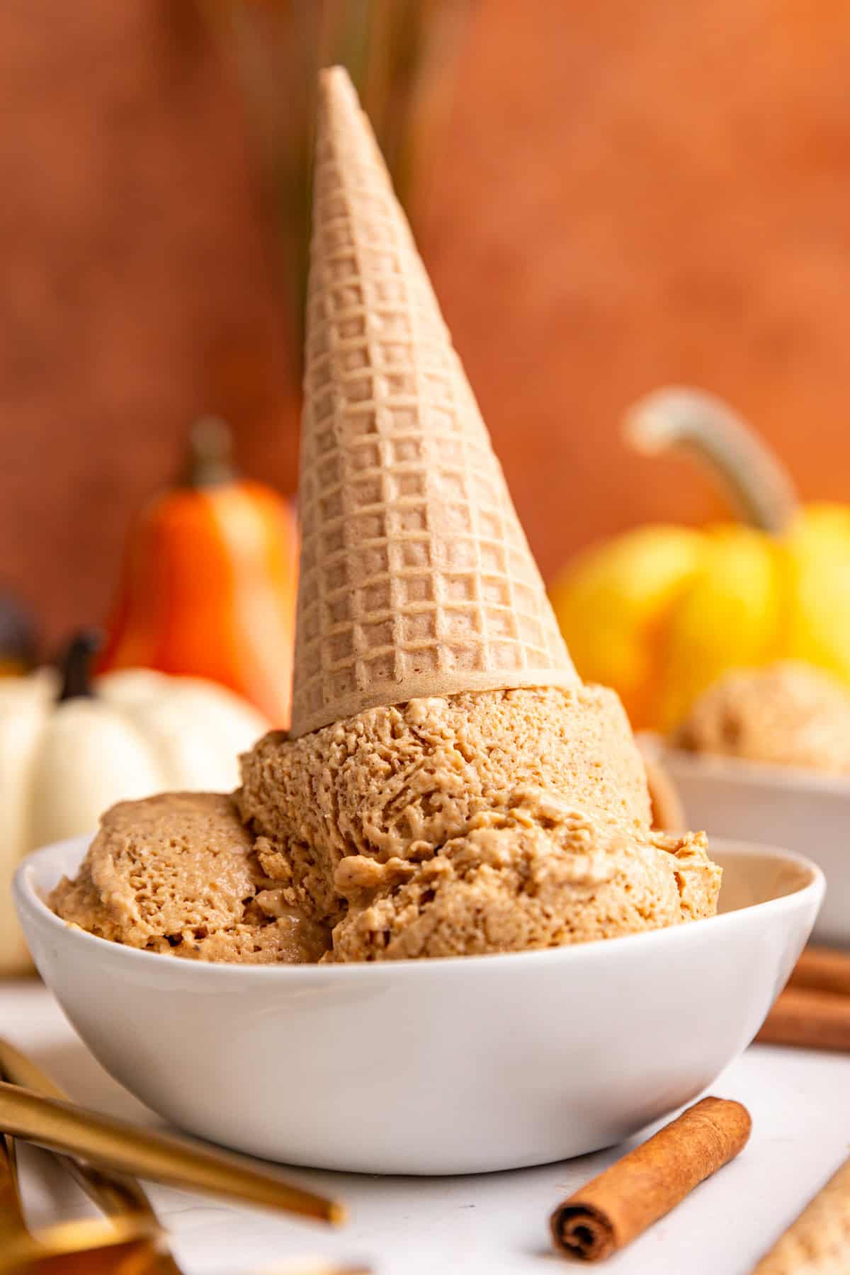 A bowl of several scoops of vegan pumpkin pie ice cream, with an ice cream cone upside down in the bowl.