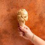 A hand holding an ice cream cone with two scoops of vegan pumpkin pie ice cream.