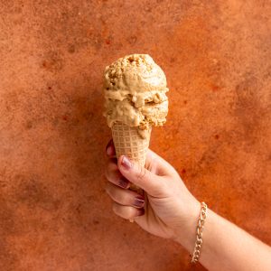 A hand holding an ice cream cone with two scoops of vegan pumpkin pie ice cream.