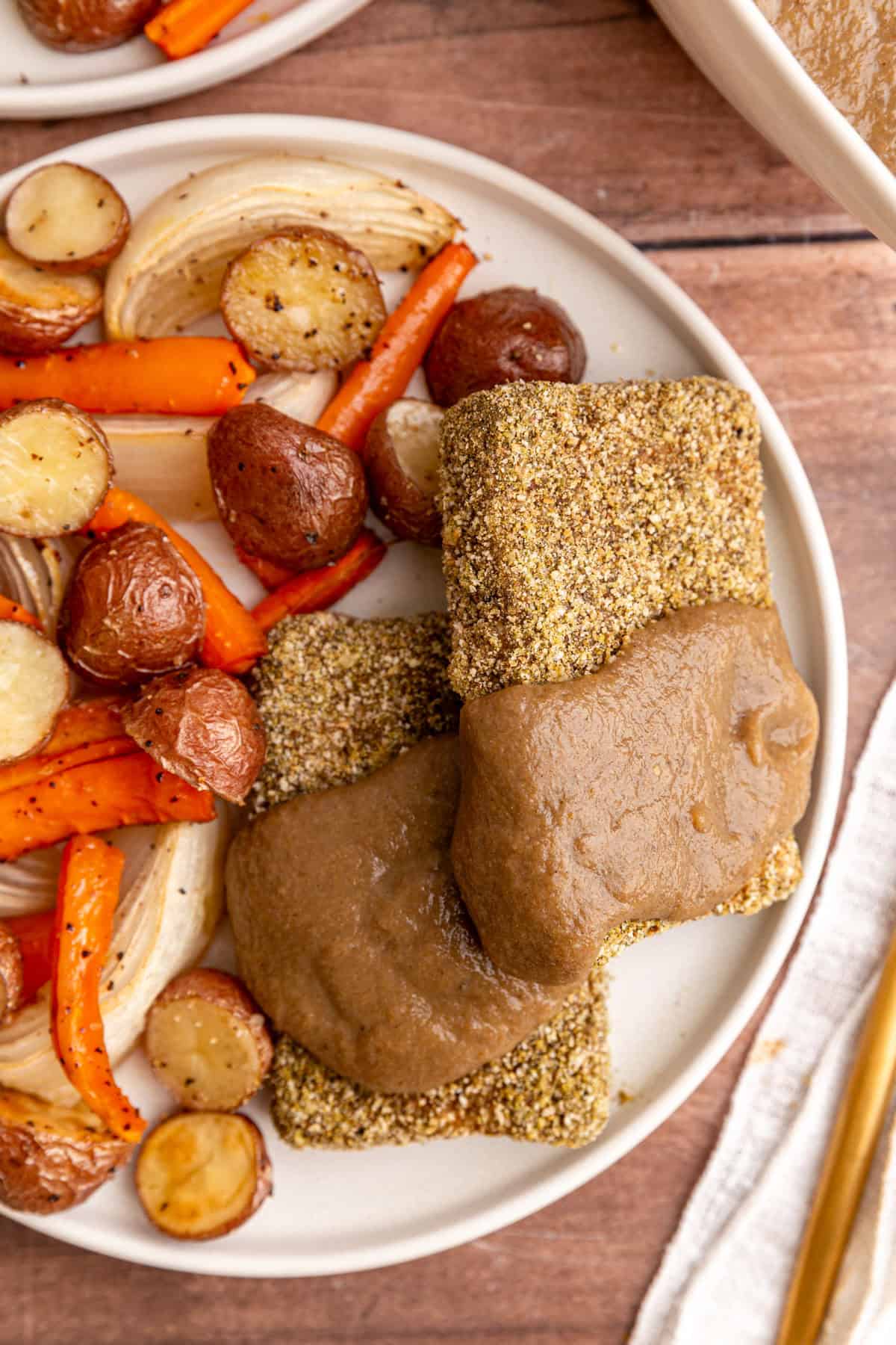 A plate of roasted vegetables and two slices of baked herb tofu, topped with gravy.