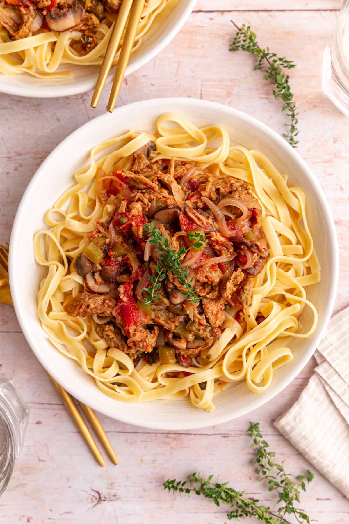 A bowl of Vegan Cacciatore served over pasta, garnished with fresh thyme.