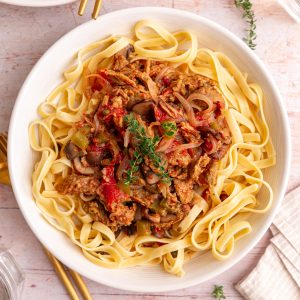 A bowl of Vegan Cacciatore served over pasta, garnished with fresh thyme.