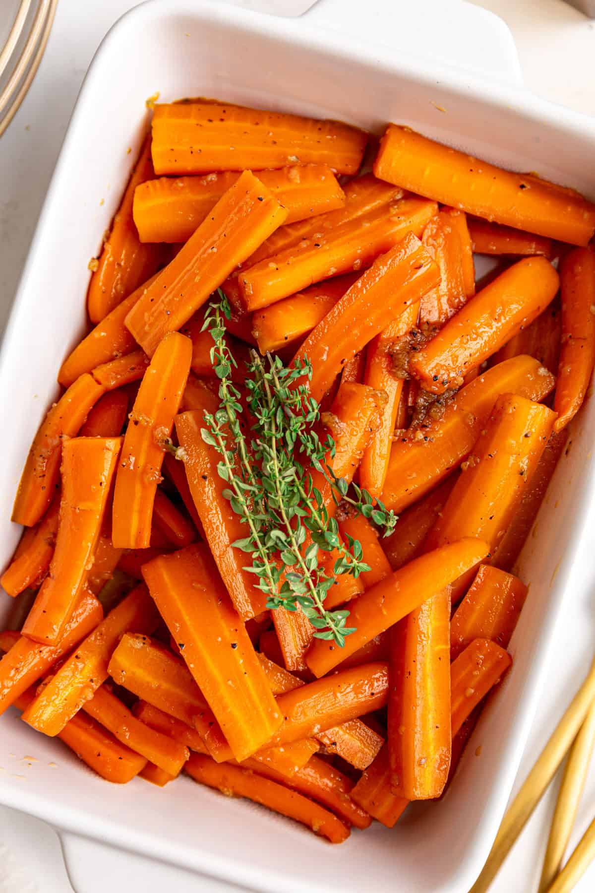 A dish of vegan glazed carrots, with a large bunch of thyme on top.