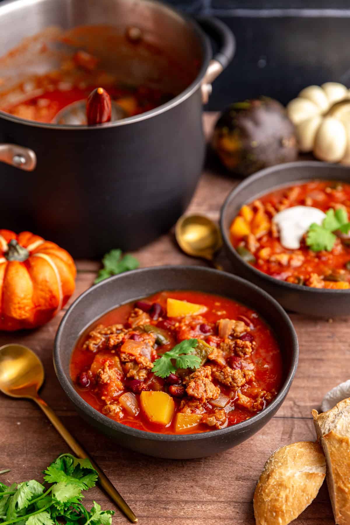 Several bowls of pumpkin chili with the pot of chili and a ladle.