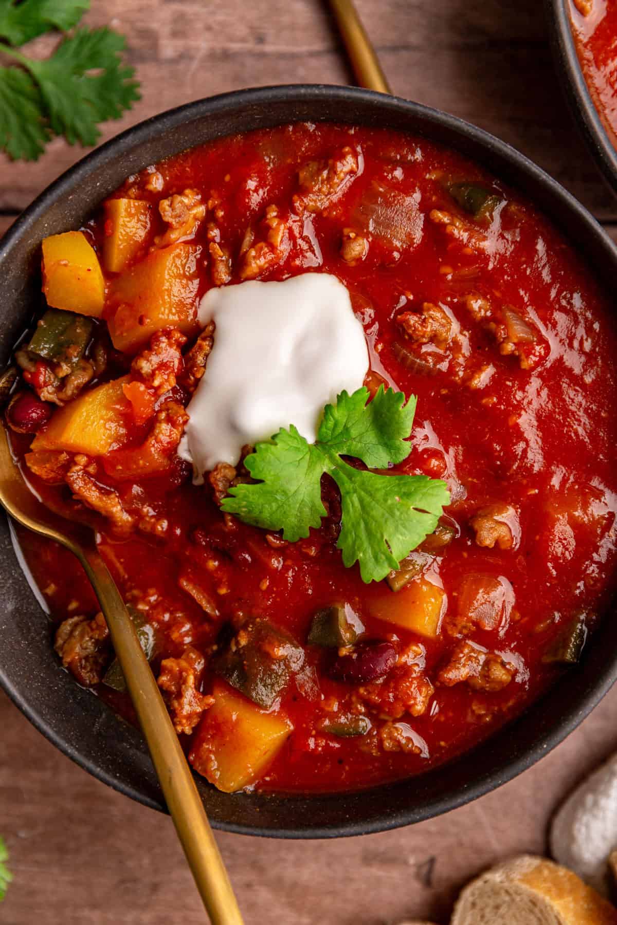 A bowl of Vegan Pumpkin Chili, garnished with cilantro and yogurt, with a spoon, ready to eat.