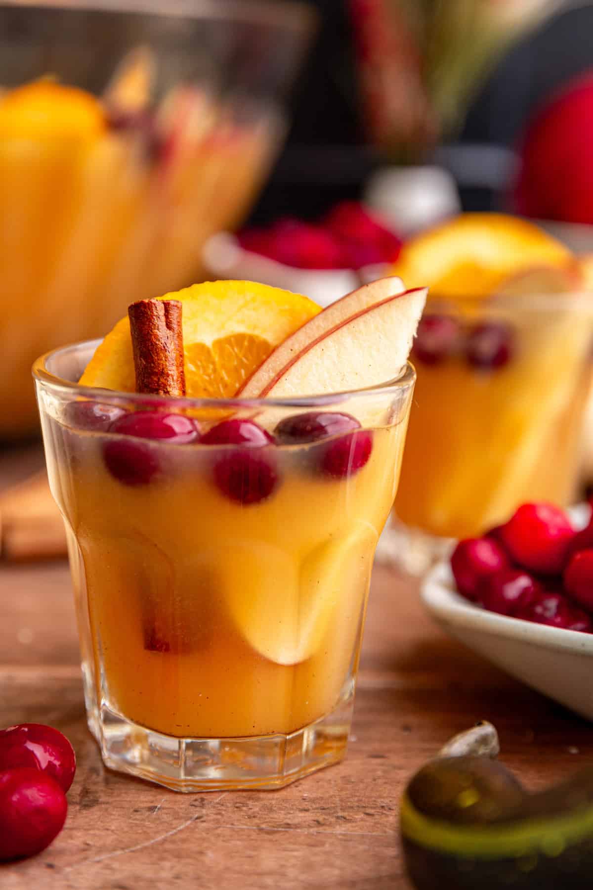 A glass of punch, garnished with an orange slice, apple slices, cranberries, and a cinnamon stick.