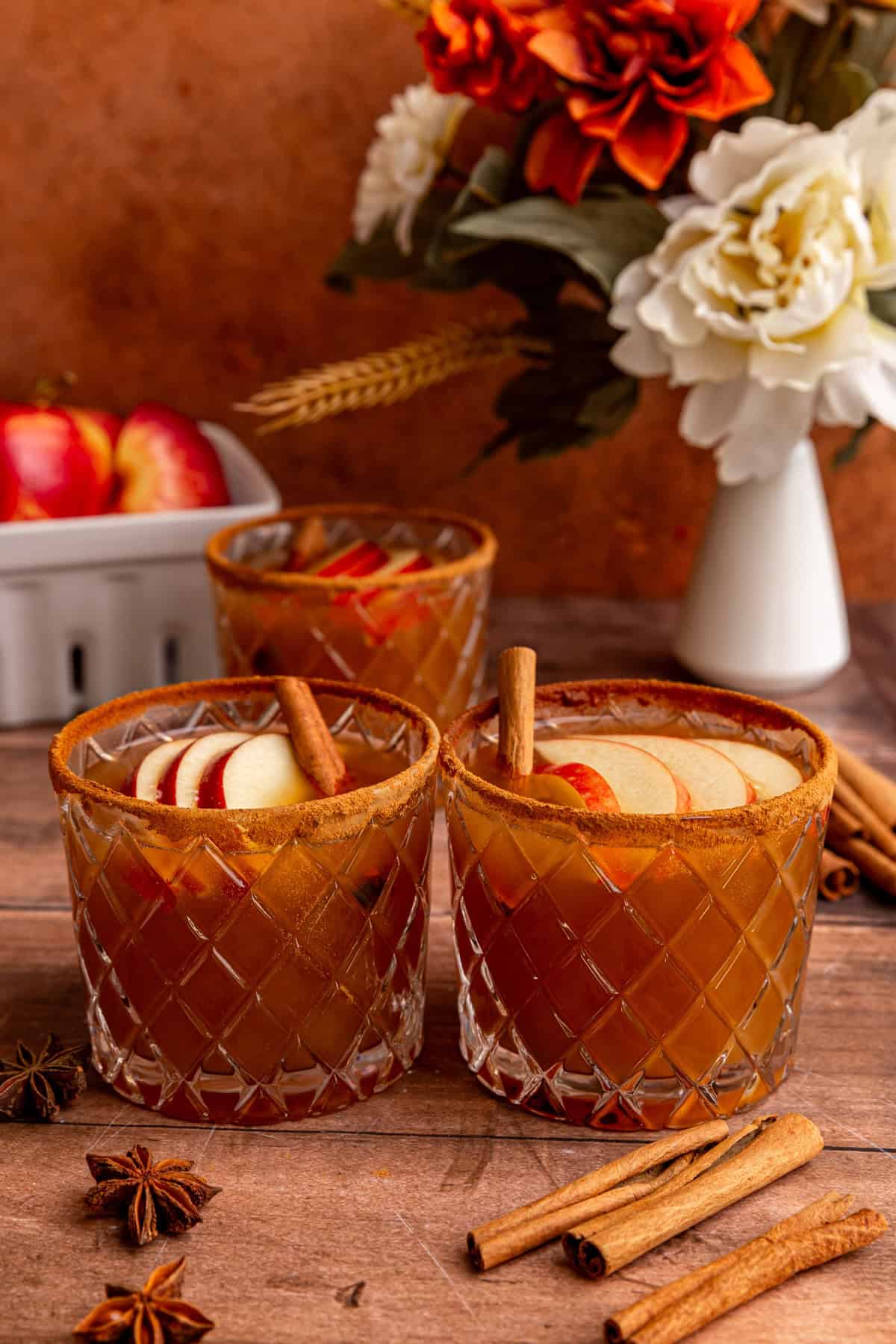 Two glasses of Thanksgiving mocktail, garnished with cinnamon sticks and apple slices.