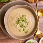 A bowl of vegan celery soup, garnished with scallions and hemp seeds.
