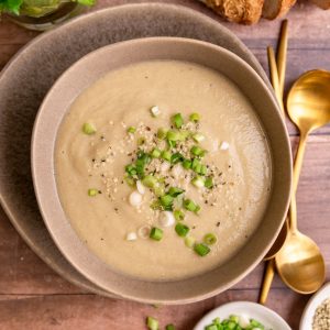 A bowl of vegan celery soup, garnished with scallions and hemp seeds.